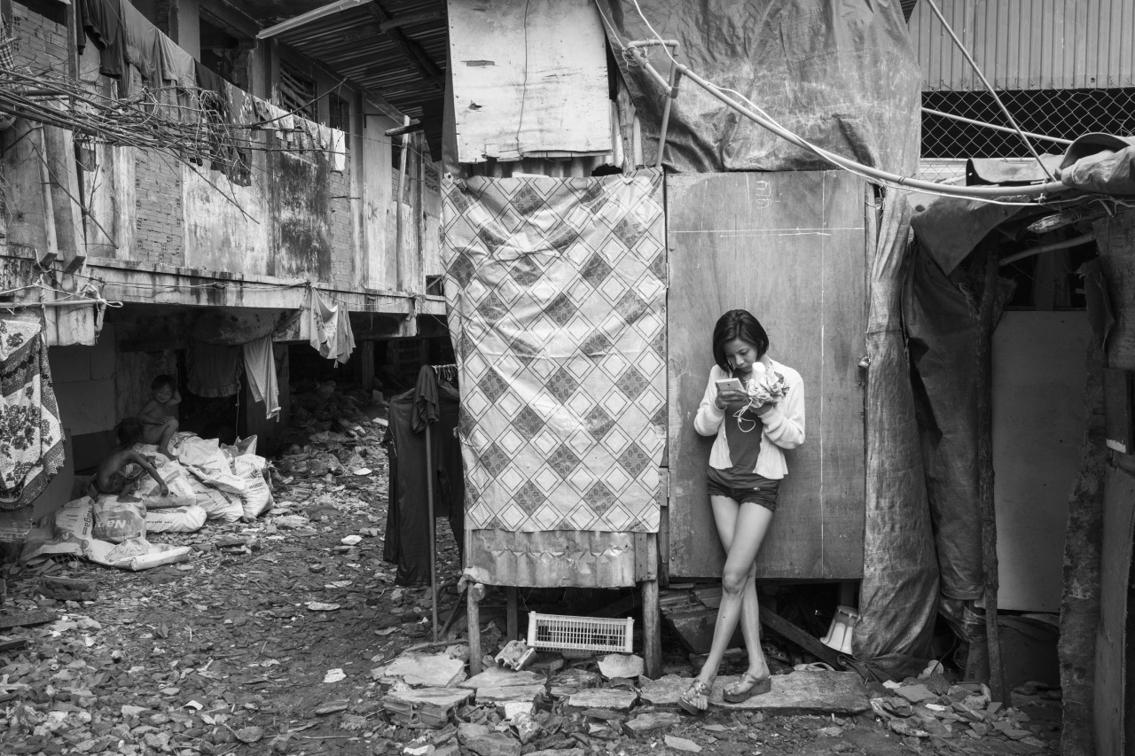 CAMBODIA, Phnom Penh. 3/12/2014: Young girl checking her smartphone in the unhealthy settlement which grew at the foot of the buildings which were promised to the Borei Keila community before their violent eviction on January 2012.